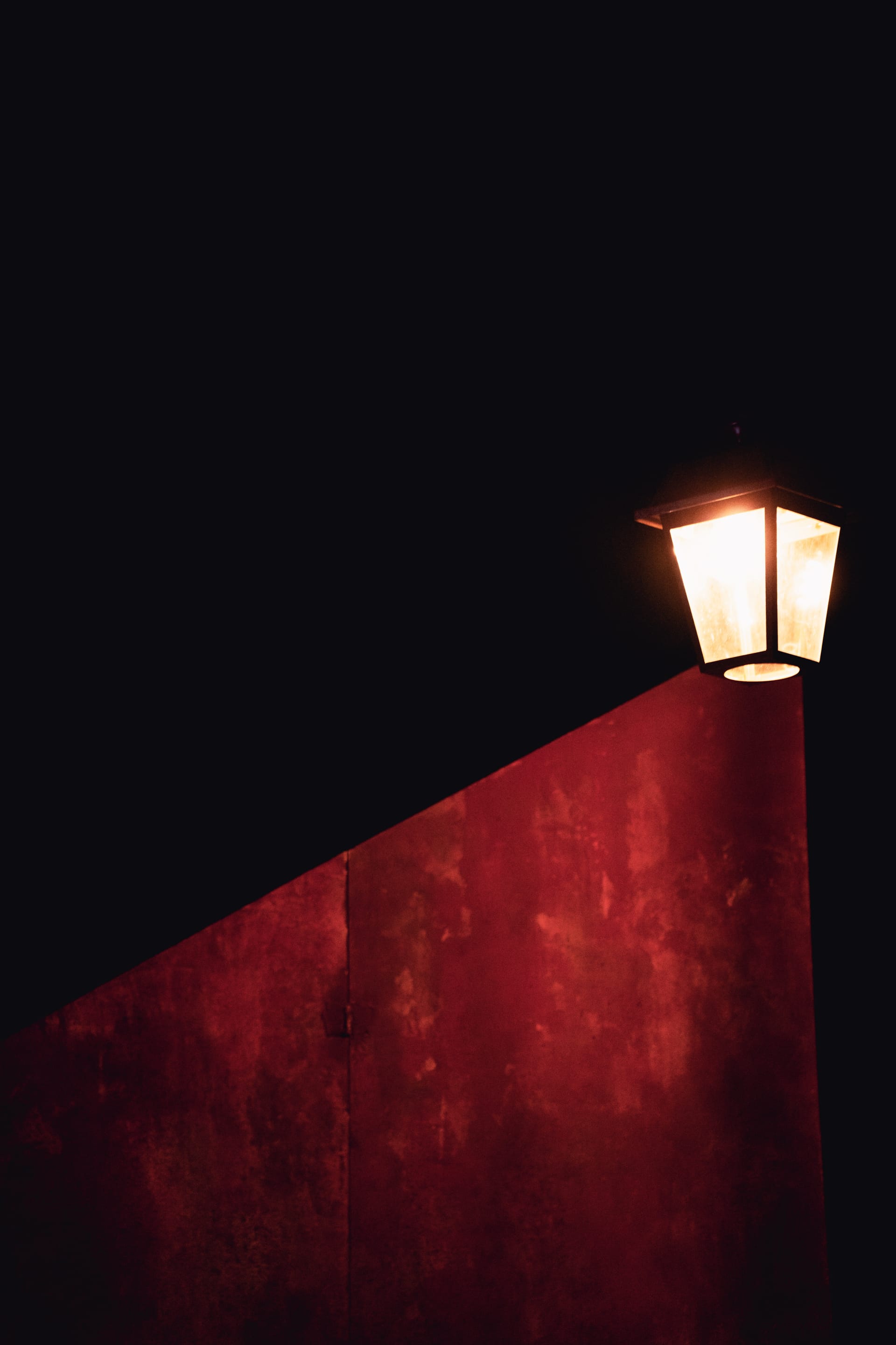 Un réverbère à gaz allumé sur un mur rouge, dans la nuit de Whitechapel